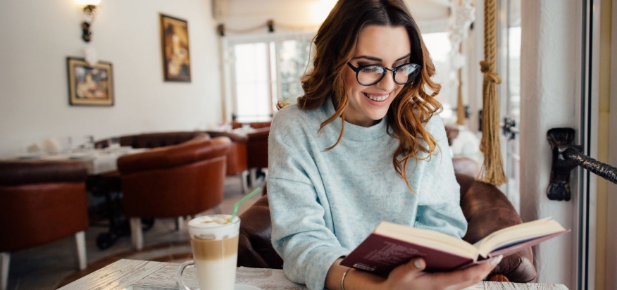 A Young Lady With Beautiful Smile On her Face While Reading A Book.