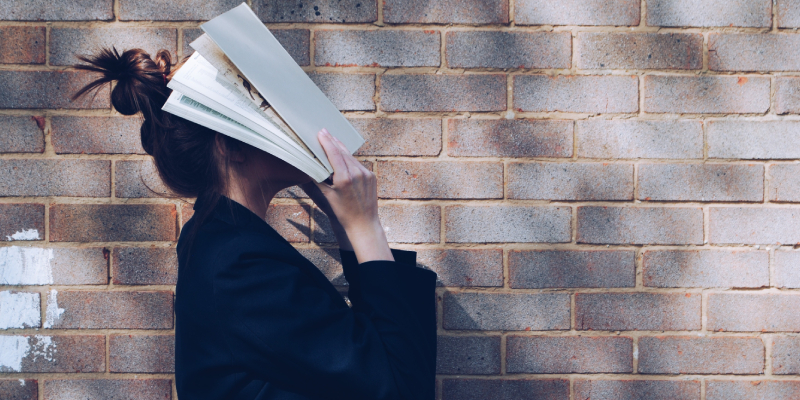 A Young lady Hide Her Face With A Book About Entreprenaur In A Brick Background.