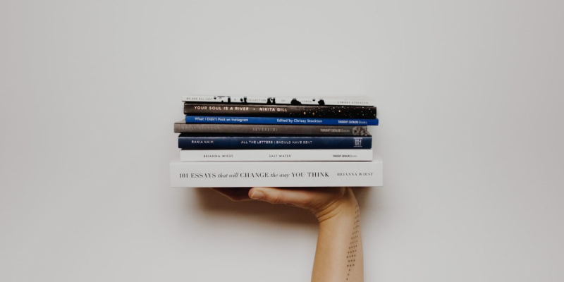 A Pile Of Books About Branding That Has Holding By A Human Hand In A White Background.