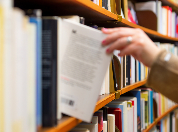 A Person Taking A Book About Marketing From The Stack Of Books In The Library.