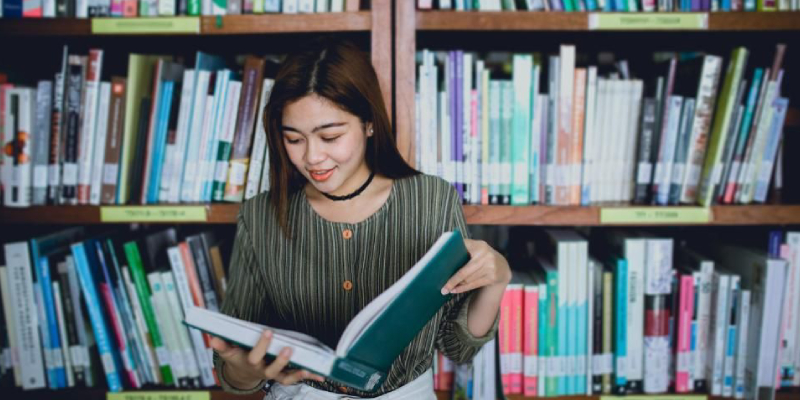 A Young Lady Opened And Read A Book In A Library.